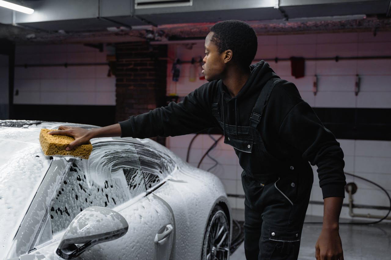 gallery-1 A person washing a car with a sponge, deep cleaning in a garage setting.